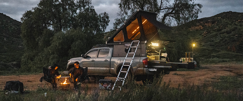 Overland Toyota Tacoma with rooftop tent deployed and Total Chaos long travel suspension, set up for remote camping and off-grid adventure travel